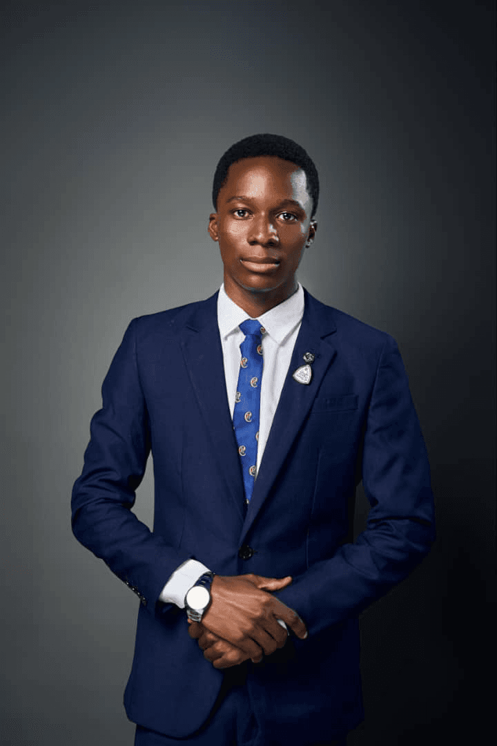 Mathias Bala, in a navy suit and blue tie, photographed against a grey studio background.
